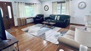A spacious living room with a ceiling fan, a sofa, a coffee table, and a TV stand. - Green Acres (Minford)
