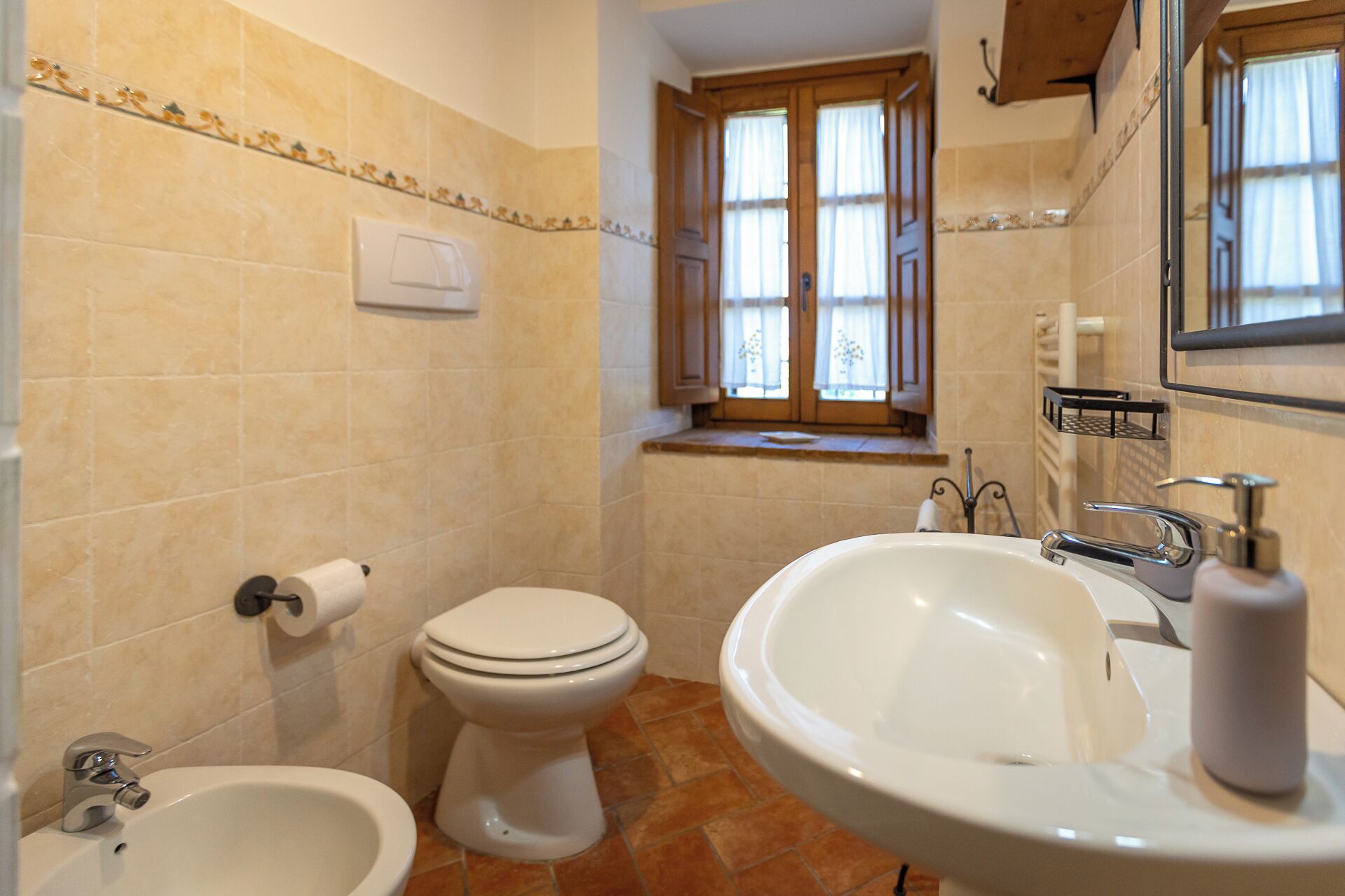 A bathroom with a toilet, bidet, sink, and window.