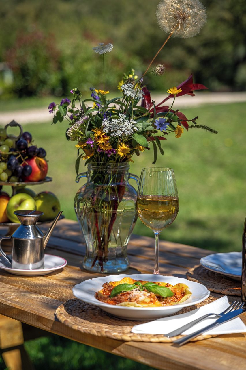 Una mesa servida con comida, una copa de vino, un florero y una jarra de agua.