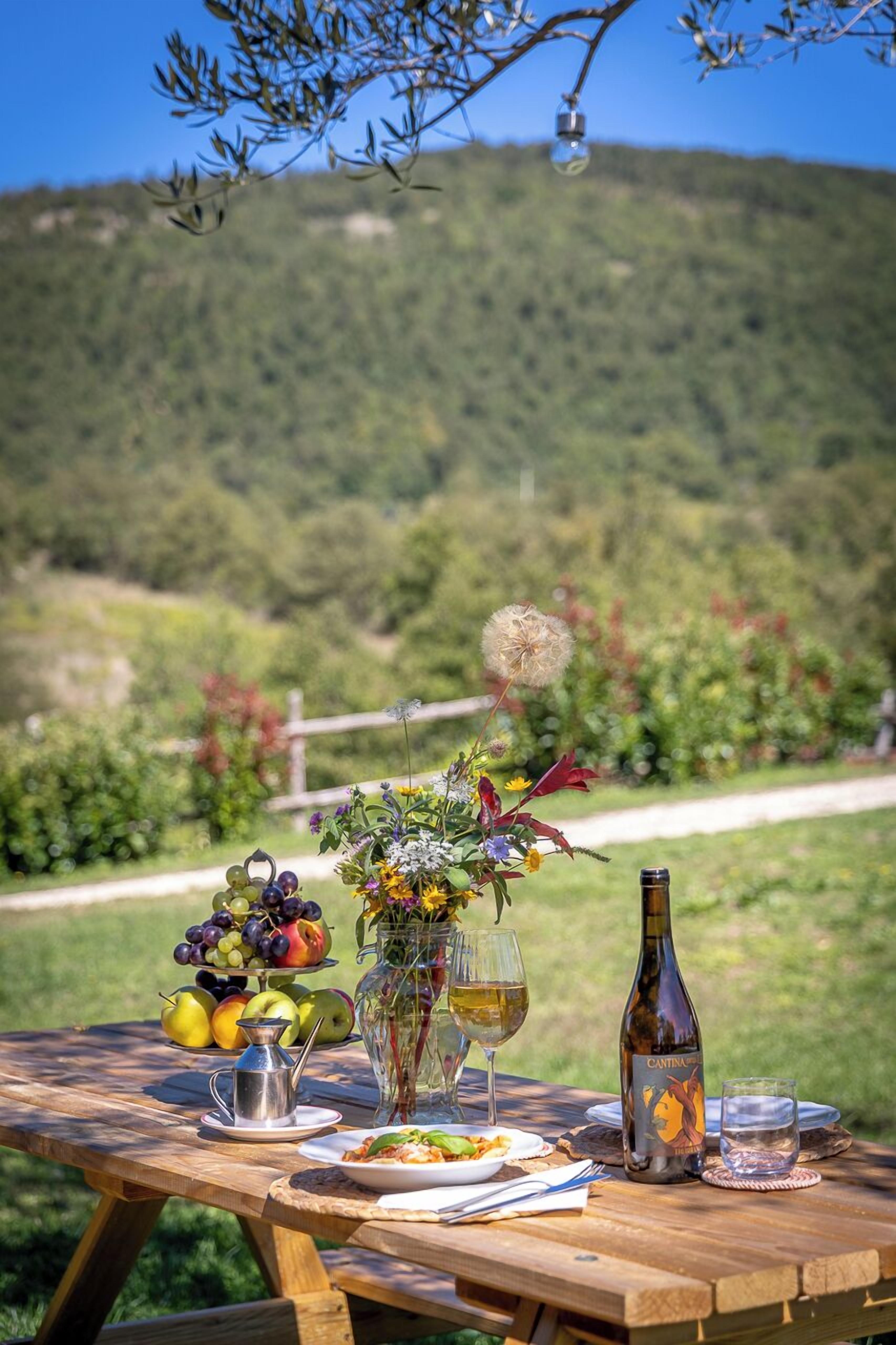Ein Picknick mit einer Flasche, Weingläsern und einer Obstkomposition auf einem Holztisch.