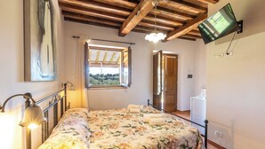 A bedroom with a bed, a TV mounted on the wall, a window with curtains, and a door leading to another room.