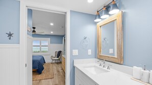 Ein Badezimmer mit weißem Waschtisch, einem großen Spiegel und einem Deckenventilator.