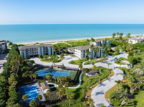 Un complexe hôtelier comprenant plusieurs bâtiments, un court de tennis et offrant une vue sur la plage.