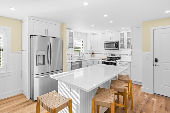 A modern kitchen with white cabinetry, stainless steel appliances, and a central island with stools.