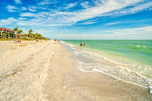 A beach with clear turquoise water, a sandy shore, and a few people in the distance.