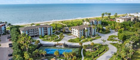 A resort with multiple buildings, a tennis court, and a beach view.
