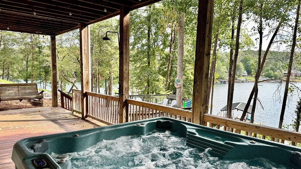 Een hottub op een houten terras met uitzicht op een meer en bomen.