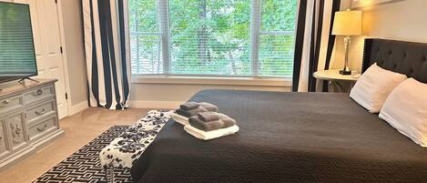 A bedroom with a large bed, a dresser, a window with blinds, a lamp, and a ceiling light.
