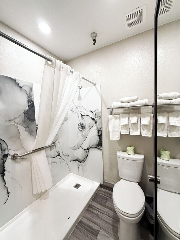 Une salle de bain moderne avec un mur de douche en marbre, une baignoire blanche, des toilettes et un porte-serviettes avec des serviettes pliées.