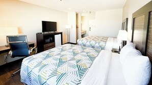 Una habitación de hotel con cama, escritorio con computadora, televisor y espejo.