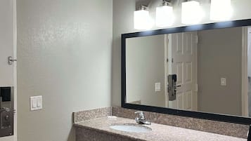 Un baño con encimera de granito, un lavamanos, un espejo y una puerta.