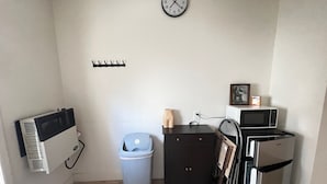 A compact kitchen with a clock, a trash bin, a microwave, and a refrigerator.