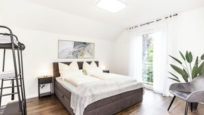 Une chambre à coucher avec un lit, des tables de chevet, une échelle, une grande fenêtre avec des rideaux et une plante.