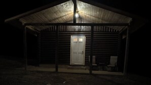 Una cabaña de madera con un porche cubierto, un brasero al frente y una puerta al fondo.