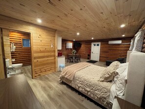 A log cabin bedroom with a bed, a small table, and a chair.