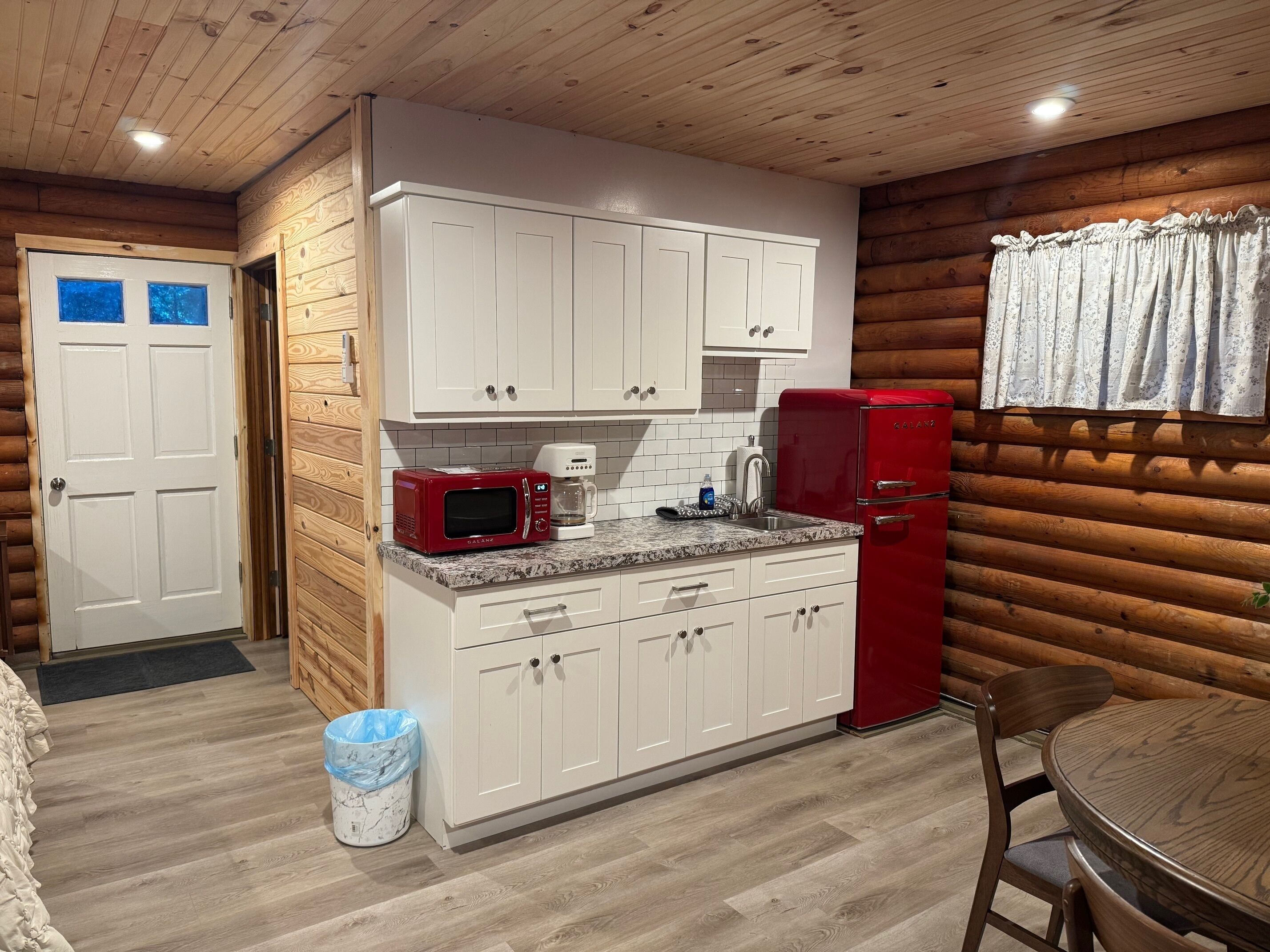 A compact kitchen with white cabinets, a red microwave, and a red refrigerator.