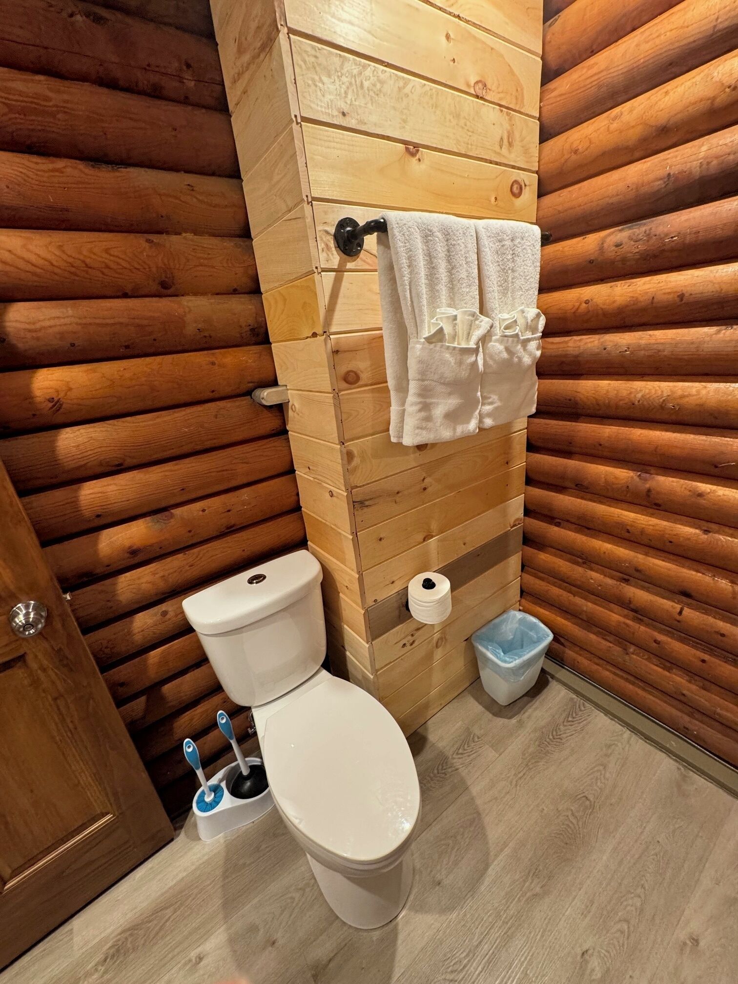 Un baño con paneles de madera, un inodoro, un perchero para toallas y un cubo de basura.