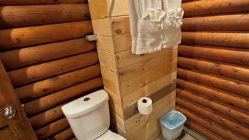 Un baño con paneles de madera, un inodoro, un perchero para toallas y un cubo de basura.