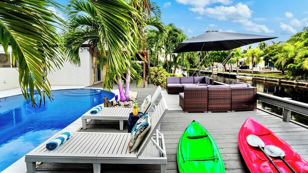 Un espace aménagé au bord de la piscine, avec des chaises longues, une table à manger et des kayaks.