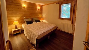 Een slaapkamer met een houten hoofdbord, een bed met een beddengoed met een patroon, twee bedlampen en een raam met gordijnen.