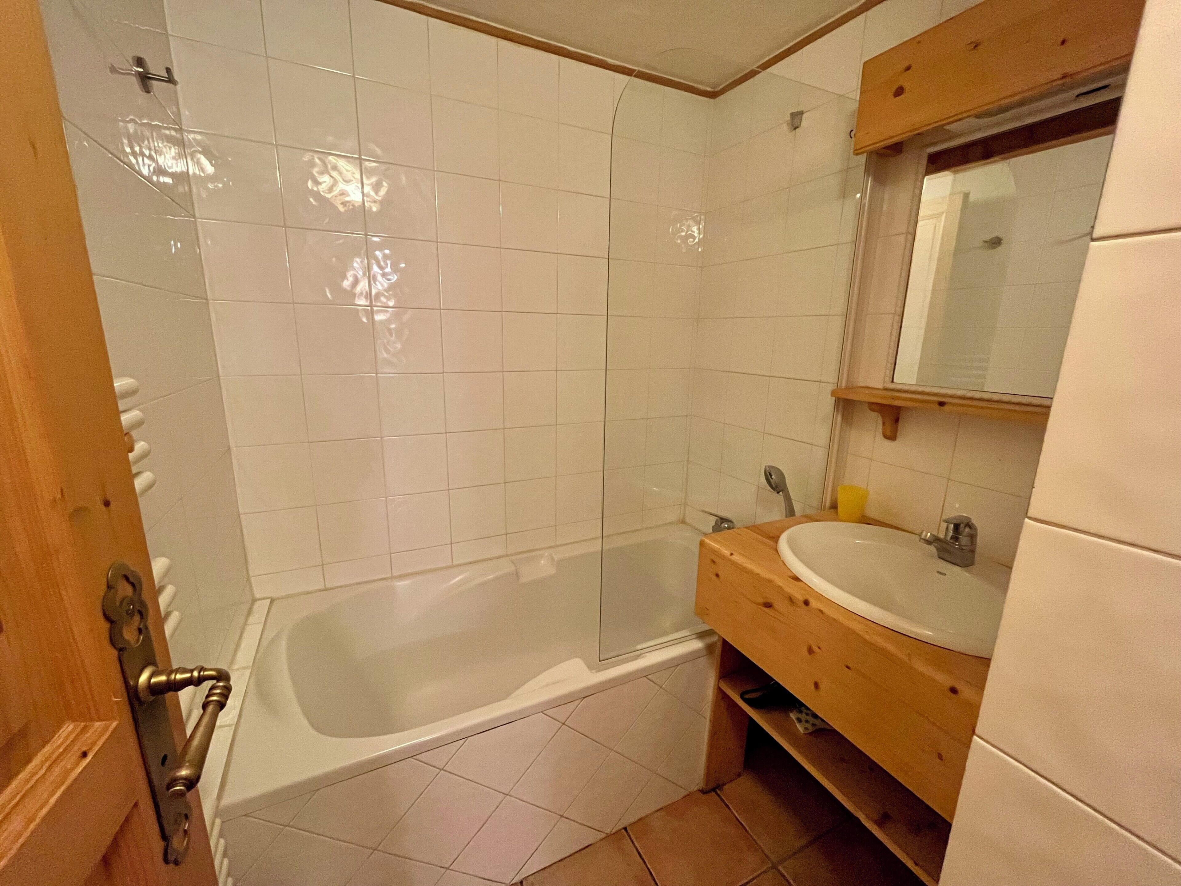 A bathroom with white tiles, a wooden vanity, a sink, and a bathtub.