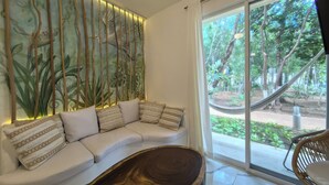 A modern living room with a white sofa, patterned cushions, a wooden coffee table, and a large window with a view of a hammock and greenery outside. - 2be 2ba, Playa del Carmen. Ground floor. Free early check in and late check out. (Playa del Carmen)