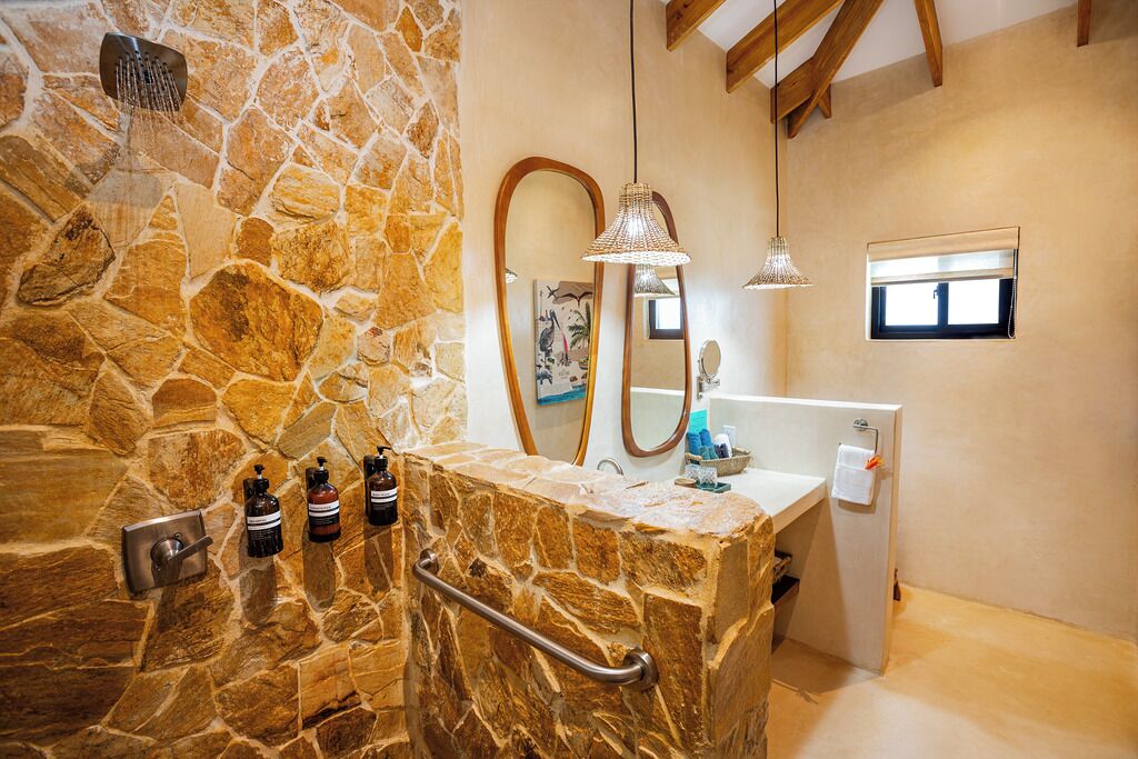 Ein Badezimmer mit Steinwand, Dusche, Waschtisch mit Spiegel und einer Pendelleuchte.