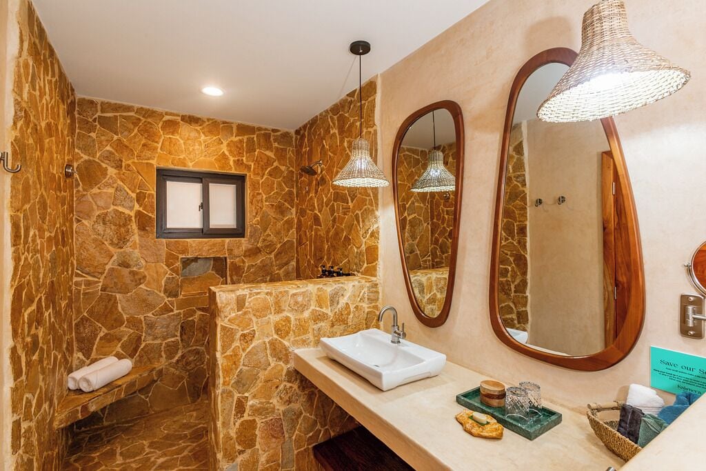 Un bany amb parets de pedra, un lavabo, dues làmpades penjants i un mirall gran.