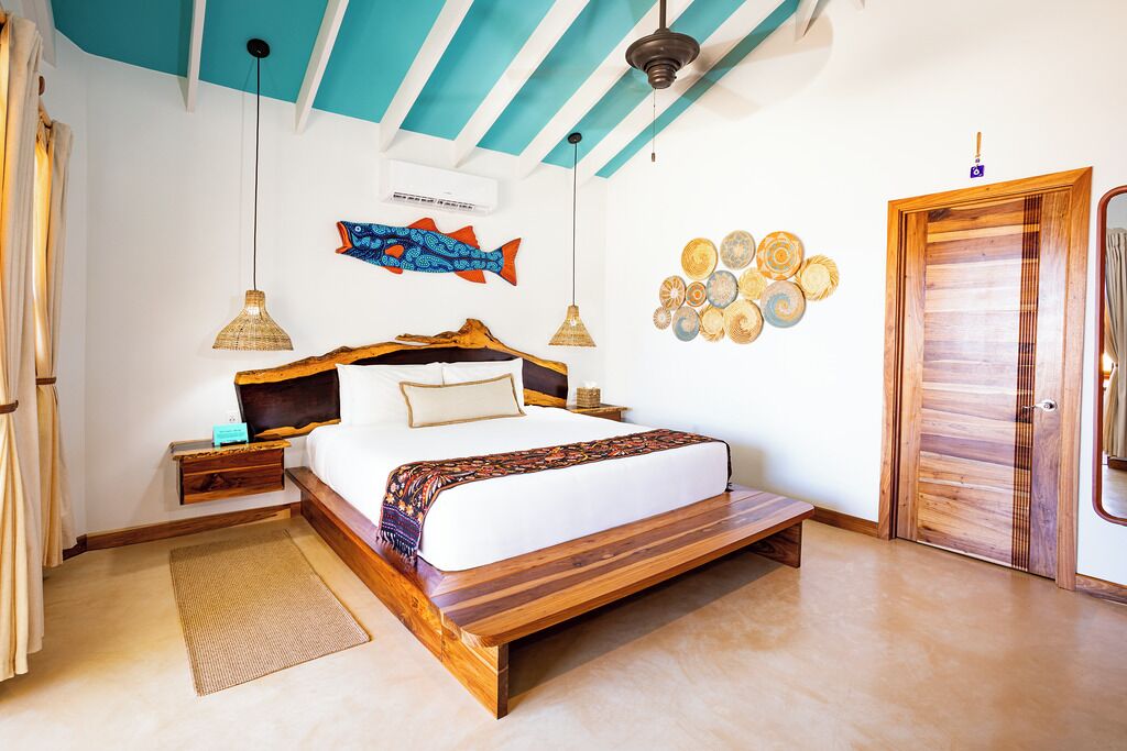 A bedroom with a wooden bed, a ceiling fan, a wall-mounted fish decoration, and a wooden door.