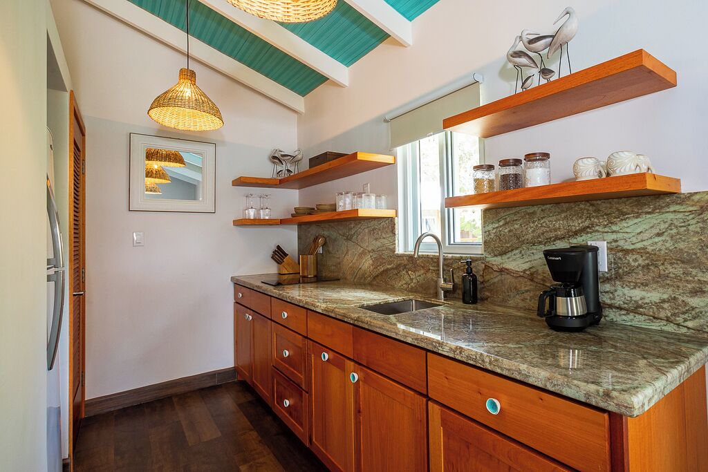 A kitchen with wooden cabinets, a granite countertop, a coffee maker, and a hanging light fixture.