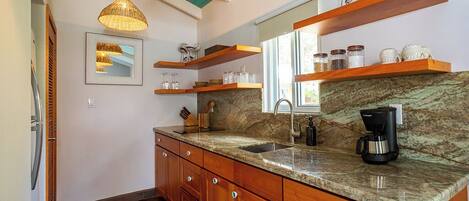 A kitchen with wooden cabinets, a granite countertop, a coffee maker, and a hanging light fixture.