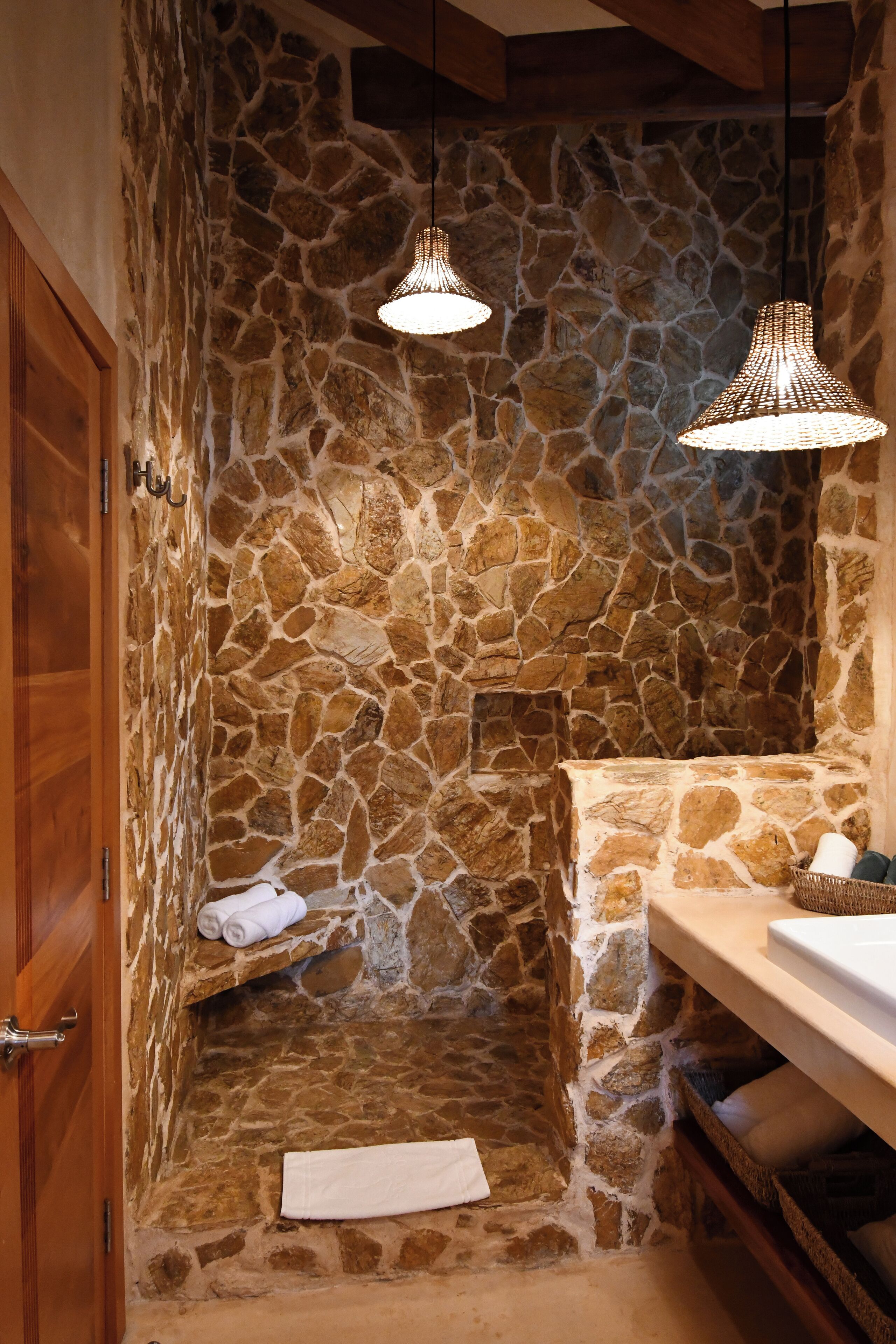 A stone-walled bathroom with a wooden door, a sink, and two hanging pendant lights.