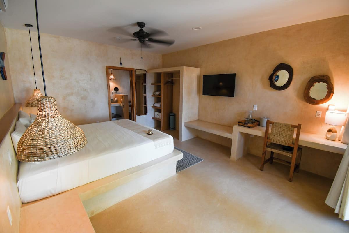 A bedroom with a bed, a desk, a chair, a ceiling fan, and a TV.