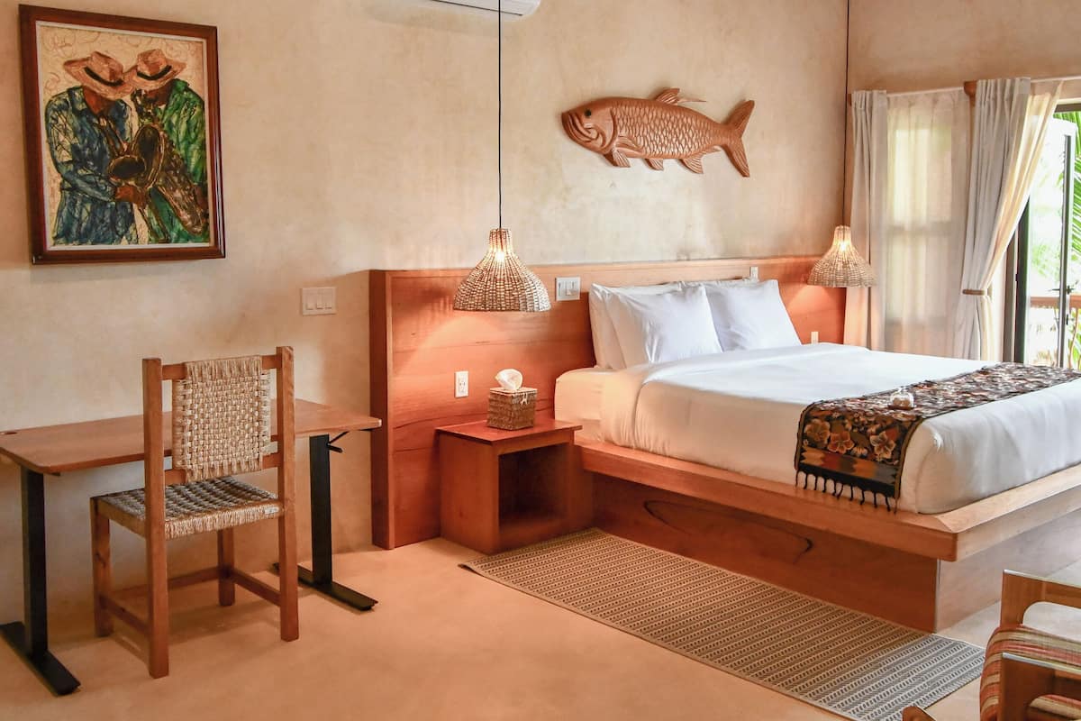 A bedroom with a bed, wooden headboard, bedside tables, a chair, a desk, and a fish wall art piece.