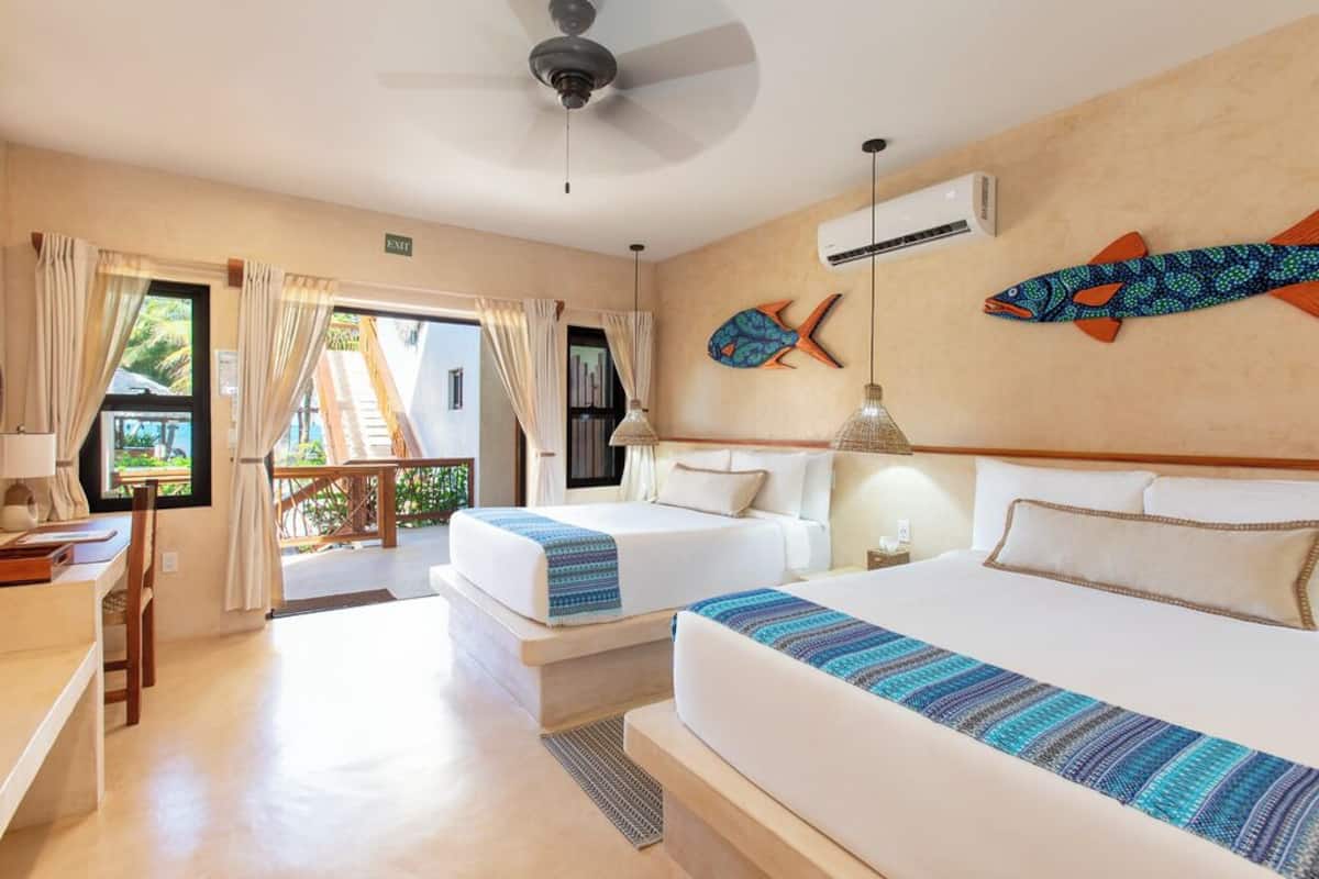 A hotel room with two beds, a desk, and a view to the outside.