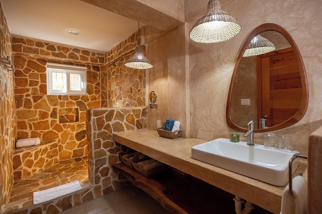 A bathroom with a stone wall, a wooden bench, a sink with a mirror, and pendant lights.