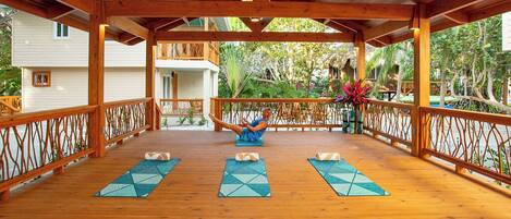 A wooden deck with yoga mats and a person doing a yoga pose.