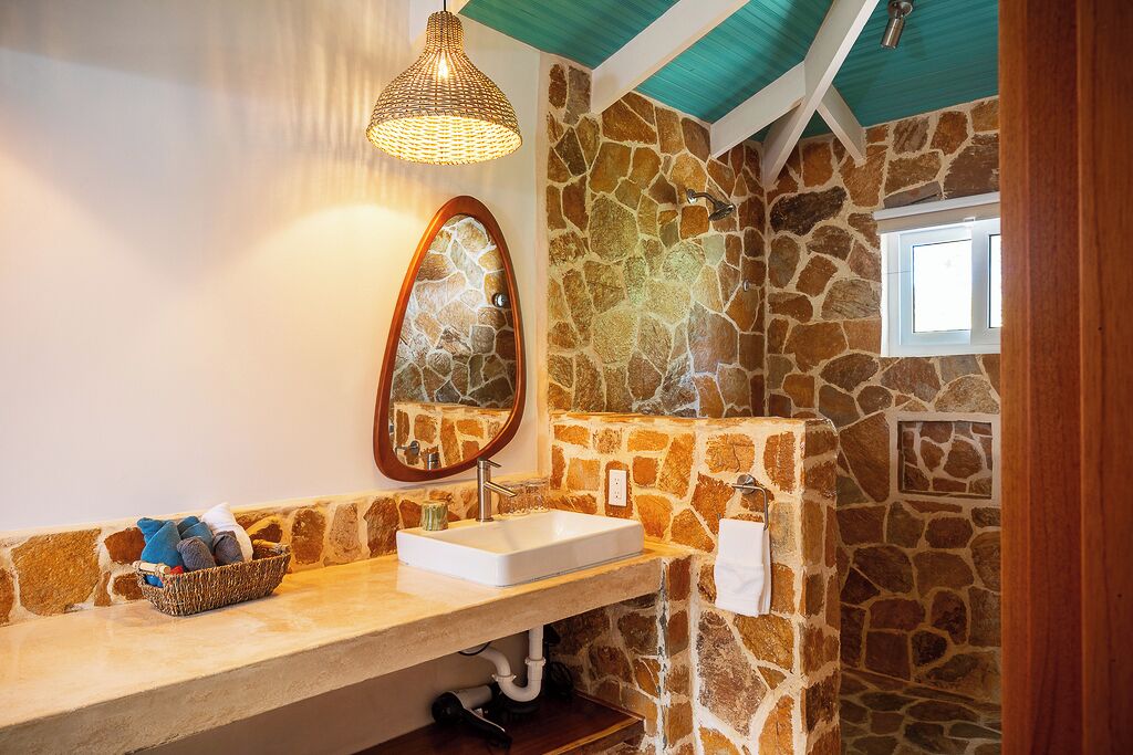 A bathroom with a stone wall, a white sink, a mirror, a towel rack, and a hanging light fixture.