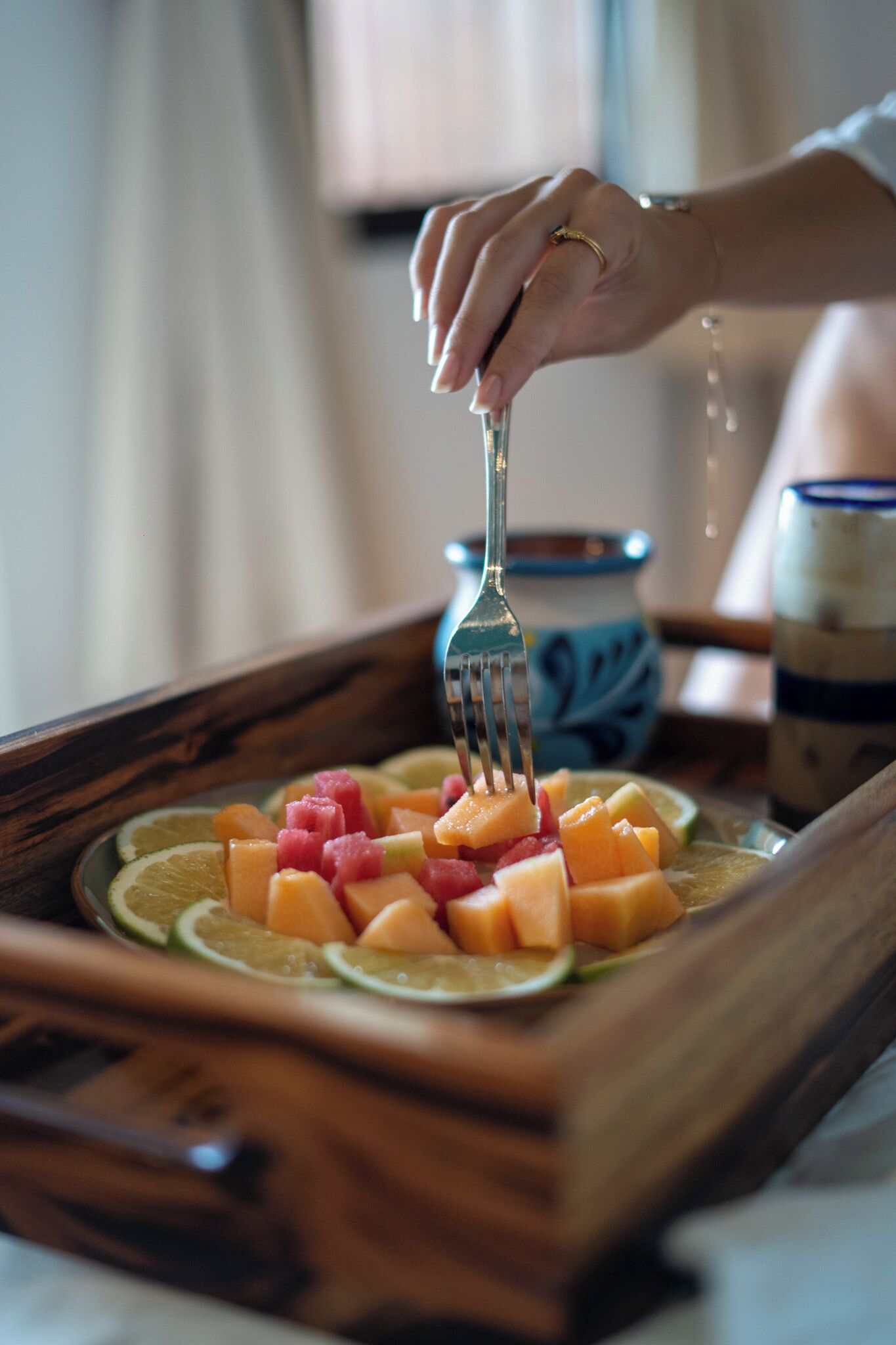 A wooden tray with sliced fruits and a hand holding a fork.
