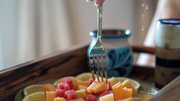 A wooden tray with sliced fruits and a hand holding a fork.