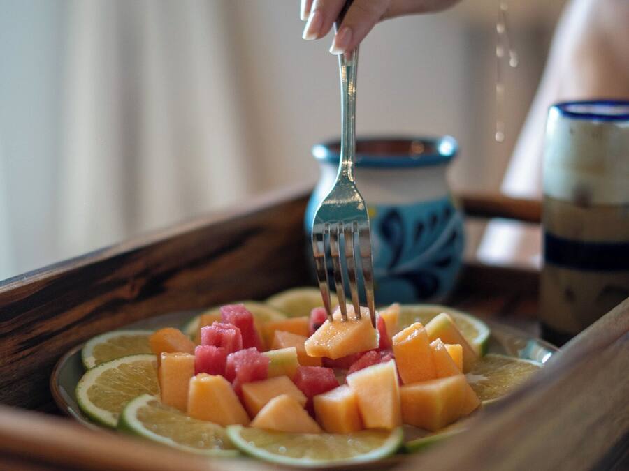 A wooden tray with sliced fruits and a hand holding a fork.