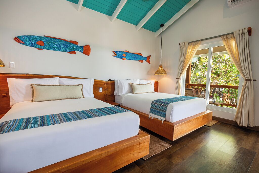 Une chambre avec deux lits, des têtes de lit en bois, une grande fenêtre avec des rideaux et des décorations murales représentant des poissons.