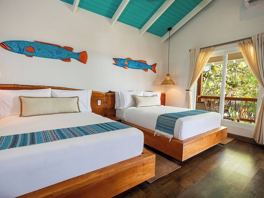 A room with two beds, wooden headboards, a large window with curtains, and wall-mounted fish decorations.
