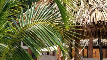 Two wooden lounge chairs with white cushions and striped pillows, positioned under a thatched roof structure on a sandy beach.