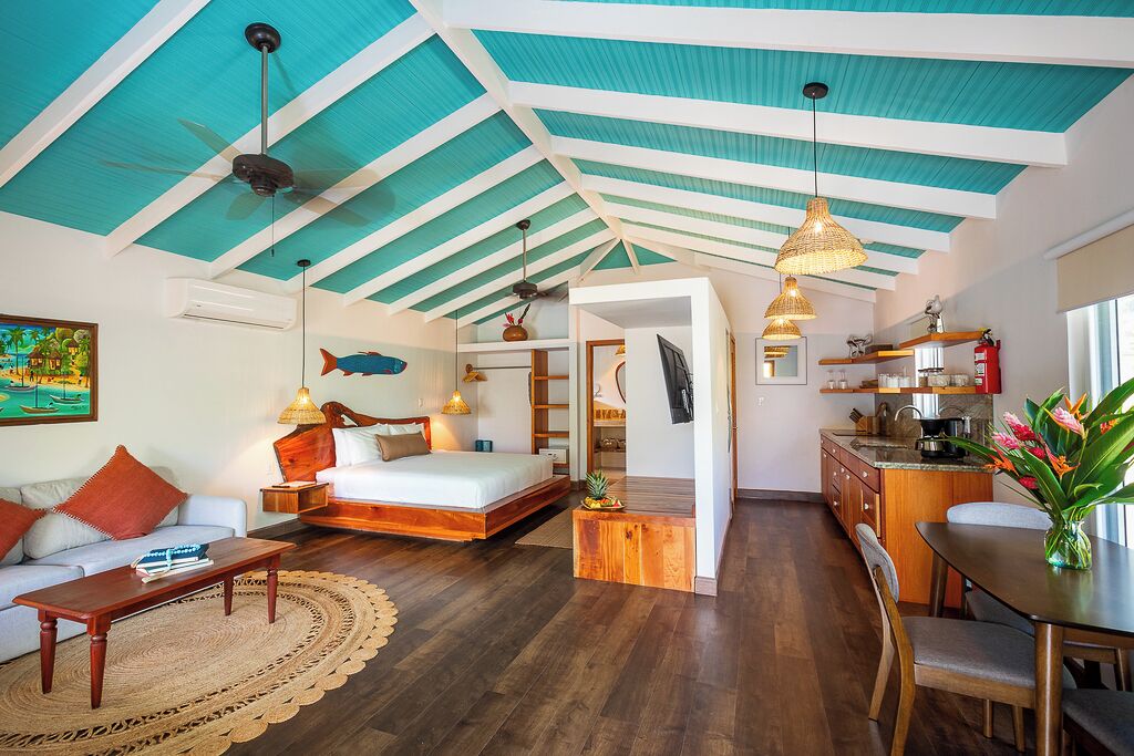 A spacious room with a bed, a sofa, a dining table, and a kitchen area.