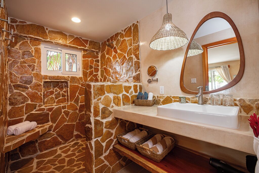 A bathroom with a stone wall, a white sink, a mirror, and a hanging light fixture.
