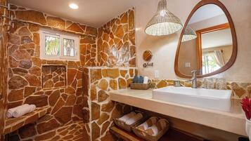 A bathroom with a stone wall, a white sink, a mirror, and a hanging light fixture.