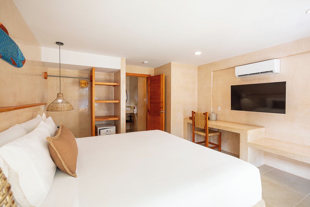 Una habitación de hotel moderna con una cama grande, un escritorio con silla, un televisor montado en la pared y un armario.