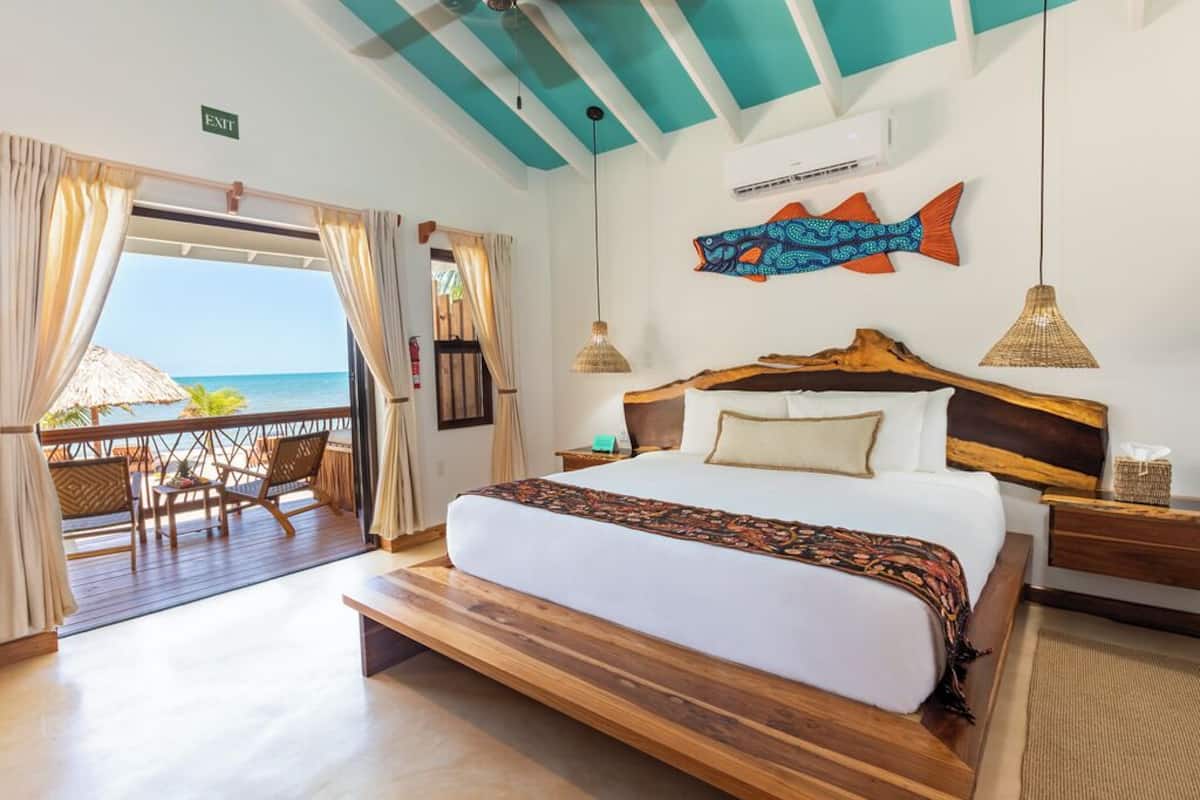 A hotel room with a large bed, wooden headboard, and a view of the ocean.