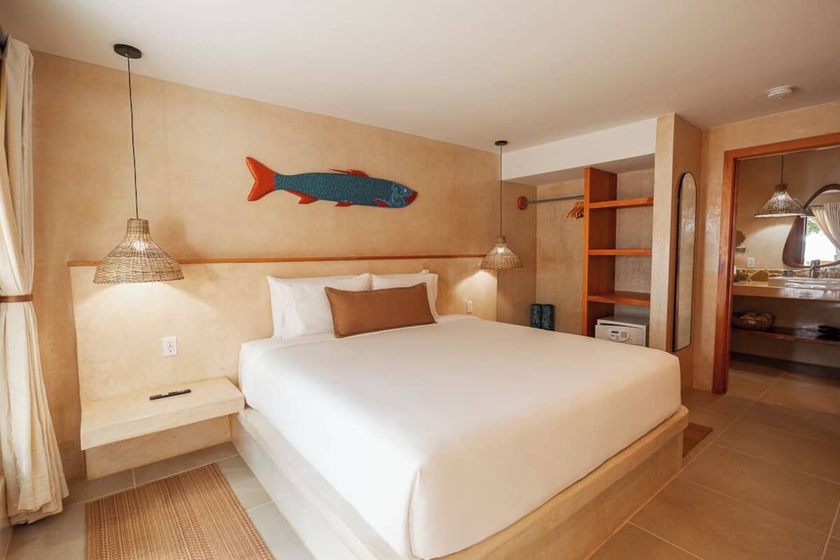 A bedroom with a large bed, bedside lamps, a fish wall art, and a wooden shelf unit.